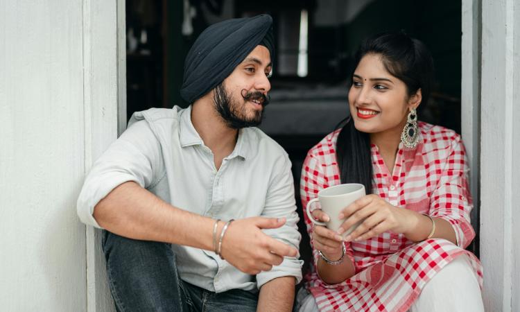 An Indian man and woman sitting chatting as she holds a cup of tea