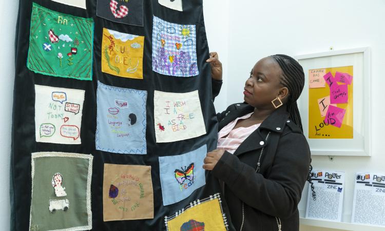Mary hangs a textiles artwork on the wall at the Our Power exhibition